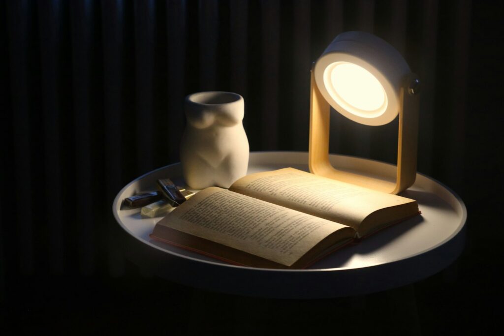 E-reader met een opengeslagen boek op een tafel naast een leeslamp